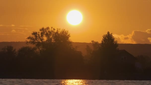 Lakeside landschap met donker silhouet van park bomen weerspiegeld in meer water en ver lopen voetgangers op dijk bij heldere zonsondergang — Stockvideo