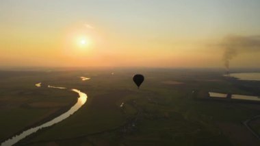 Gün batımında kırsal alanda uçan büyük sıcak hava balonu manzarası.