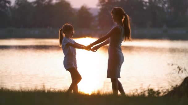 Happy mom and daughter girl relaxing holding hands enjoying time together in summer park at sunset. Family love and relationship concept — Stock Video