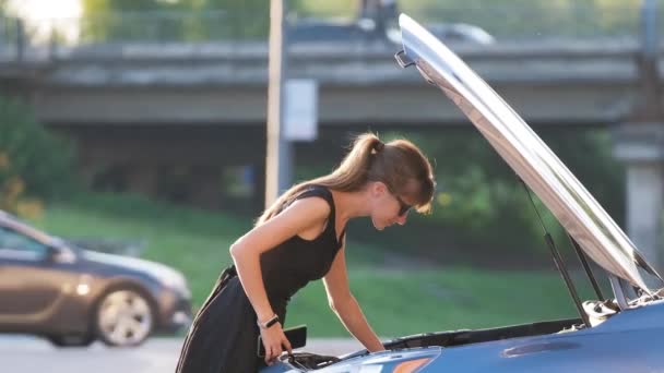 O femeie neajutorată în picioare lângă mașina ei, cu capota deschisă, apelând la serviciul de telefonie mobilă pentru ajutor. Șofer tânăr care are probleme cu vehiculul — Videoclip de stoc