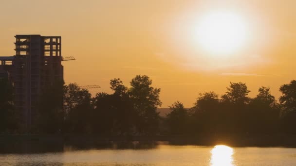 Paesaggio lacustre con silhouette scura di edifici edilizi riflessi nell'acqua del lago e lontani pedoni a piedi su argine al tramonto luminoso — Video Stock
