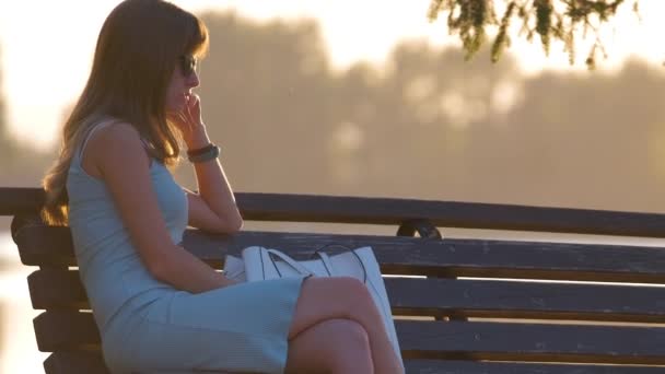 孤独な若い女性だけで湖の海岸ベンチに暖かい夏の夜を楽しんで座っている。自然の中での幸福とリラックス — ストック動画