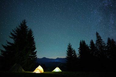 Parlak turist çadırları gece gökyüzünün altındaki karanlık dağlarda parlayan parlayan yıldızlarla. Etkin yaşam tarzı kavramı