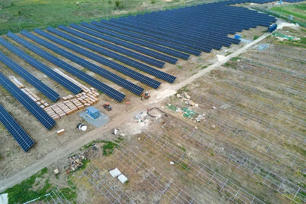 Vista aérea da grande usina elétrica em construção com muitas fileiras de painéis solares em armação metálica para a produção de energia elétrica limpa. Desenvolvimento de fontes de energia renováveis — Fotografia de Stock