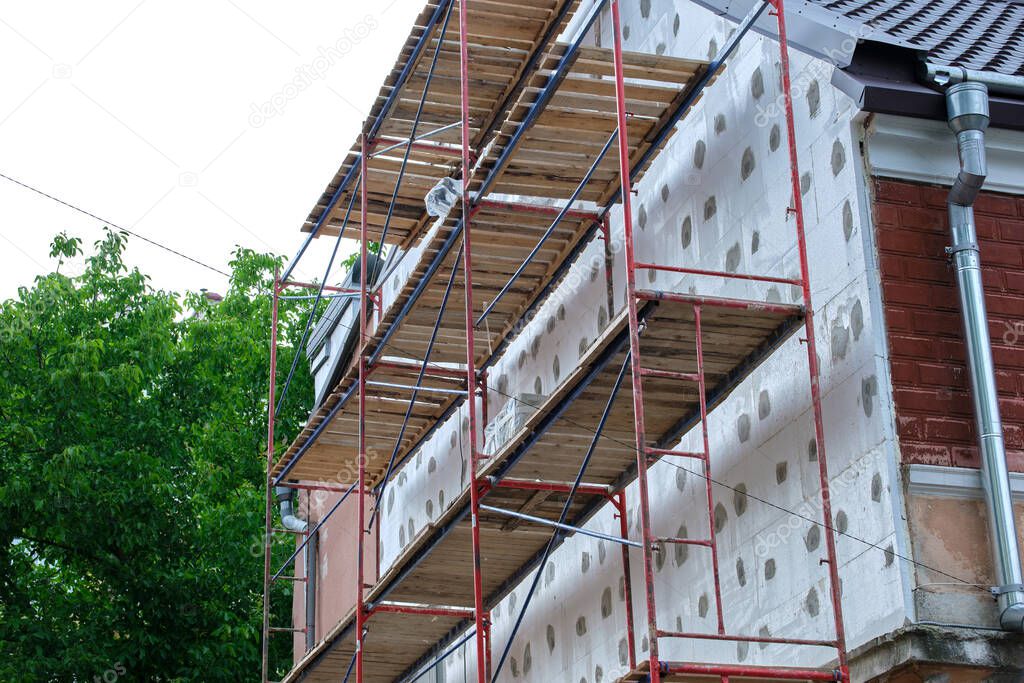 Building facade under renovation works with construction scaffolding frame. Wall insulation with styrofoam sheets for energy efficient home