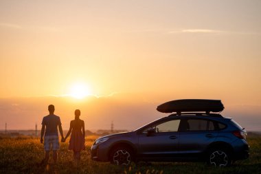 Mutlu çift sıcak yaz akşamında balayı gezileri sırasında SUV arabalarının yanında vakit geçiriyorlar. Genç adam ve kadın doğada arabayla yolculuk etmekten zevk alıyorlar.