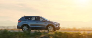 Gün batımında şehirlerarası yolda hızla giden bir SUV arabası. Akşamları otoyol trafiği