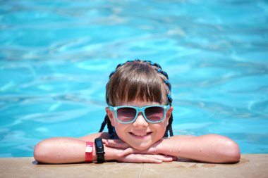 Neşeli genç kız güneşli yaz gününde açık mavi suyla havuz kenarında dinleniyor. Tropik tatil kavramı