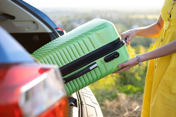 Nahaufnahme einer Frau, die einen grünen Koffer aus dem Kofferraum holt. Reise- und Urlaubskonzept — Stockfoto