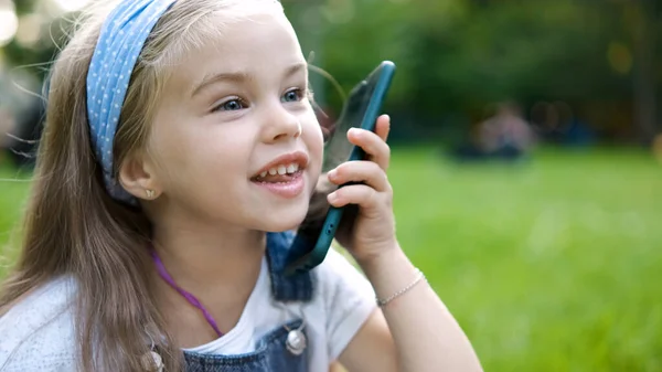 Szczęśliwe dziecko dziewczyna mówi przez telefon komórkowy w parku letnim — Zdjęcie stockowe