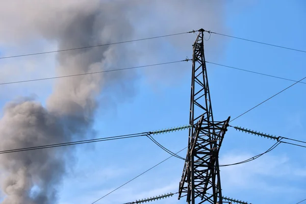 Pilones eléctricos de alto voltaje contra las tuberías altas de la central eléctrica de carbón con humo negro que se mueve hacia arriba contaminando la atmósfera. Producción de energía eléctrica con concepto de combustibles fósiles —  Fotos de Stock