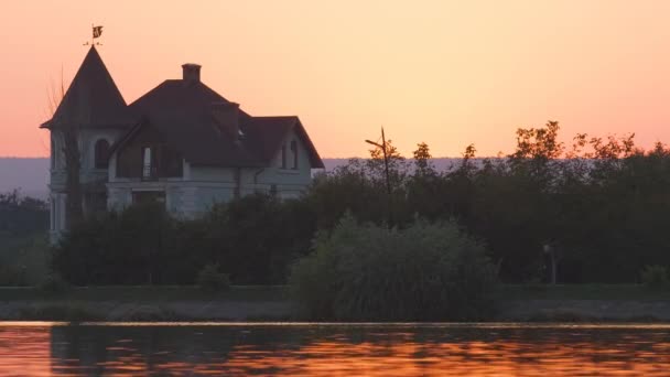 湖水前的郊区房屋和夕阳西下的路堤上远行的行人的黑暗轮廓 — 图库视频影像