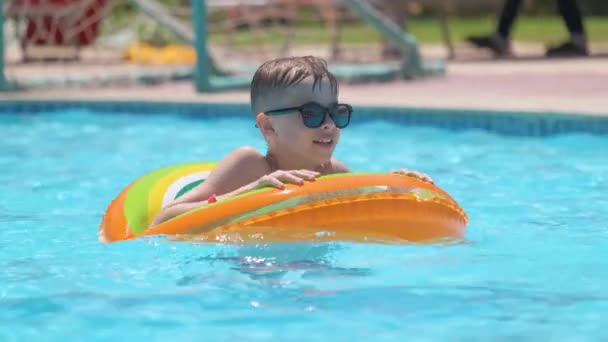 Retrato do menino feliz que relaxa no círculo inflável na piscina no dia ensolarado do verão durante férias tropicais. Conceito de atividades de verão — Vídeo de Stock