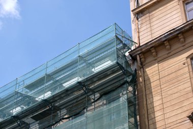 İnşaat iskelesi işçilerin güvenliği için koruyucu ağ ile örtülmüş, yenilenen binanın ön cephesi.