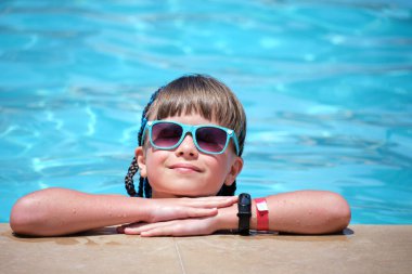 Neşeli genç kız güneşli yaz gününde açık mavi suyla havuz kenarında dinleniyor. Tropik tatil kavramı