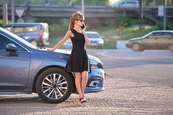 Mujer elegante conductor de pie cerca de su vehículo hablando por teléfono celular en la calle de la ciudad en verano — Foto de Stock