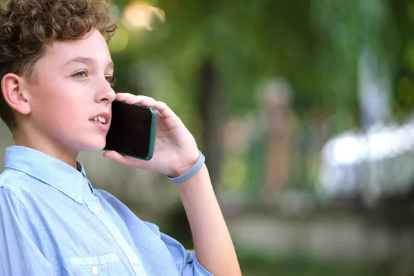 Joven niño desconcertado hablando en el teléfono celular al aire libre en el parque de verano — Foto de Stock