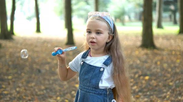 Petite fille heureuse enfant soufflant des bulles de savon à l'extérieur dans un parc vert. Concept d'activités d'été en plein air — Photo