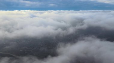 Yağmurdan önce oluşan kabarık kümülüs bulutlarıyla kaplı uzak şehrin yüksek irtifasından hava manzarası. Bulutlu manzaraya uçak bakışı
