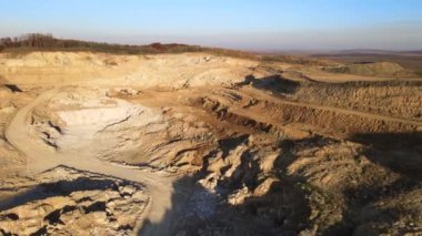 Kazı makineleri ve çöp kamyonlarıyla inşaat endüstrisi için kumtaşı malzemelerinden oluşan açık maden manzarası. Madencilik ve kullanışlı mineral üretiminde ağır ekipman
