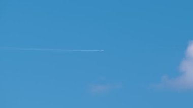 Uzaktaki yolcu uçağı mavi gökyüzünde yüksek irtifada uçarken beyaz bulutlar ardında iz bırakıyor. Hava yolculuğu konsepti