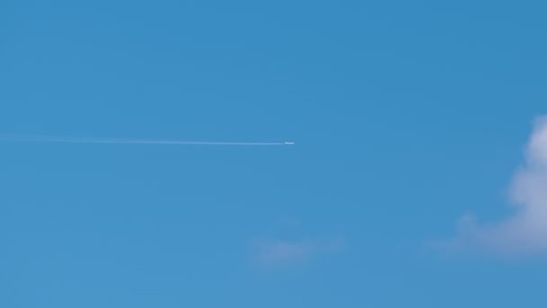 Vzdálené tryskové letadlo létající ve vysoké nadmořské výšce na modré obloze s bílými mraky zanechávajícími za sebou stopy po kouři. Koncept cestování letadlem — Stock video