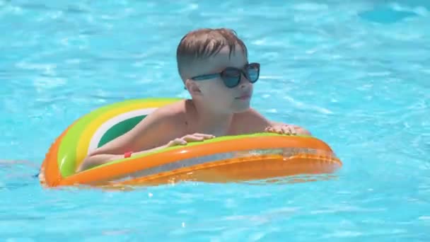 Niño feliz nadando en círculo inflable en la piscina en el día soleado del verano durante las vacaciones tropicales — Vídeo de stock