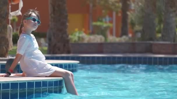Portret szczęśliwej dziewczynki w białej sukience relaksującej się na basenie w słoneczny letni dzień podczas tropikalnych wakacji — Wideo stockowe