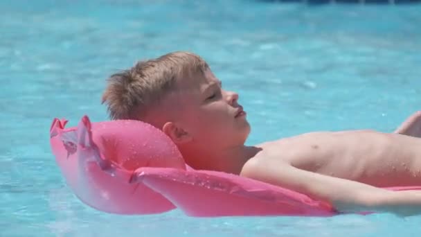 Unga barn pojke koppla av på sommaren sol simma på uppblåsbara luft madrass i poolen under tropiska semestrar. Koncept för sommaraktiviteter — Stockvideo