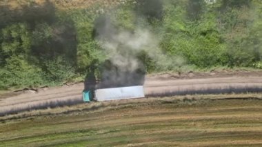 Tarımsal buğday tarlaları arasında toprak yolda giden kamyon görüntüsü. Hasat mevsiminde hasatçıların topladığı tahıl naklinden sonra.