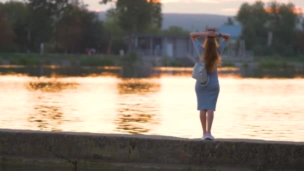 Visão traseira da mulher solitária em pé no lado do lago na noite quente. Conceito de solidão e relaxamento — Vídeo de Stock