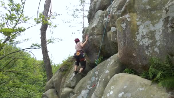 Odhodlaný horolezec šplhá po příkré stěně skalnaté hory. Sportovec překonává obtížnou cestu. Zapojení do extrémních sportů a horolezectví hobby koncept — Stock video