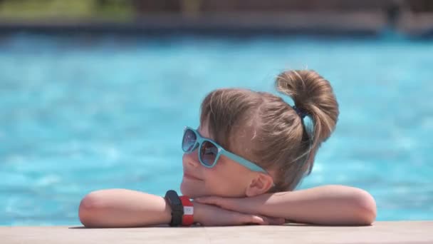 Niña feliz relajándose en el lado de la piscina en el soleado día de verano — Vídeos de Stock