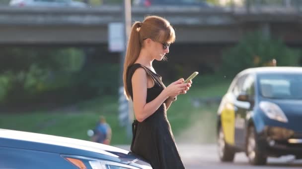 Joven conductora de pie cerca de su coche hablando por teléfono móvil en una calle de la ciudad en verano — Vídeo de stock