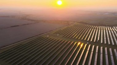 Günbatımında temiz elektrik enerjisi üretmek için birçok sıra güneş fotovoltaik paneli bulunan sürdürülebilir büyük elektrik santralinin havadan görünüşü. Sıfır emisyon kavramı ile yenilenebilir elektrik