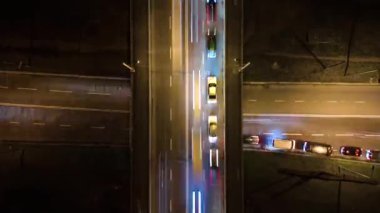 Gece yoğun trafikte hızla ilerleyen kavşağın hava görüntüsü. Şehir ulaşımının zaman aşımı. Bulanık trafik ışıkları ile trafik saati