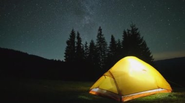 Gece yıldızlarının altındaki karanlık dağlardaki kamp alanında parlayan parlak kamp çadırının zaman atlaması. Aktif yaşam tarzı ve seyahat konsepti