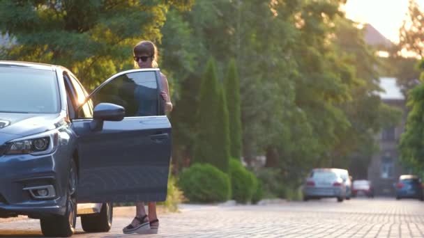 Молодая женщина-водитель выносит зеленый чемодан из машины, идущей по улице. Концепция путешествий и отдыха — стоковое видео
