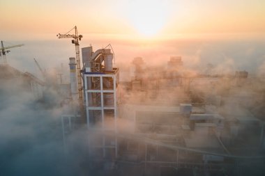 Yüksek beton yapılı çimento fabrikası ve sisli bir sabahta endüstriyel üretim alanında kule vinci. Üretim ve küresel sanayi kavramı