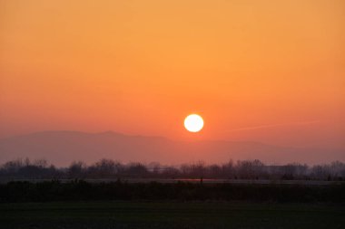 Güzel bir akşam panoramik manzarası. Gün batımında güneş batarken uzak dağ tepeleri ve asfalt yolda batıyor.