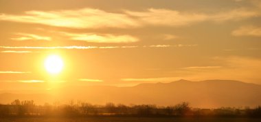 Güzel bir akşam panoramik manzarası. Gün batımında uzak dağ tepeleri üzerinde parlak batan güneş.