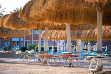 Boş güverte sandalyeleri, tropik tatil köylerinde havuz kenarında saman gölgesi şemsiyelerinin altında. Yaz tatilleri ve kaçış konsepti
