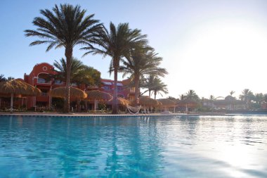 Boş güverte sandalyeleri, tropik tatil köylerinde havuz kenarında saman gölgesi şemsiyelerinin altında. Yaz tatilleri ve kaçış konsepti