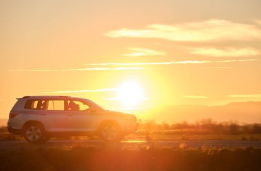 Gün batımında şehirlerarası yolda hızla giden bir SUV arabası. Akşamları otoyol trafiği