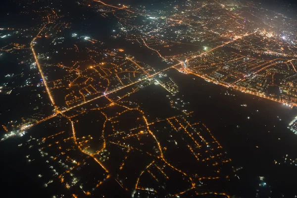 Aerial view from airplane window of buildings and bright illuminated streets in city residential area at night. Dark urban landscape at high altitude — Stock Photo, Image