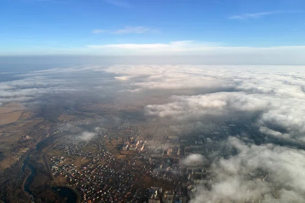 Aerial view from high altitude of distant city covered with puffy cumulus clouds flying by before rainstorm. Airplane point of view of landscape in cloudy weather — Stock Photo, Image