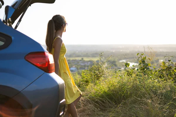 Conductora despreocupada en vestido de verano amarillo disfrutando de una cálida noche cerca de su coche — Foto de Stock