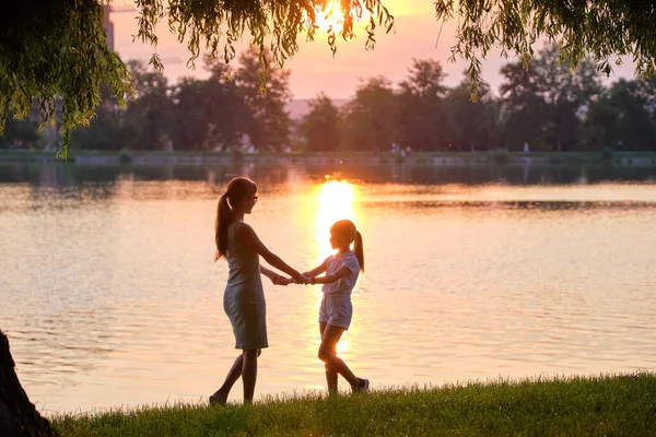 Szczęśliwa matka i córka stojące razem trzymając się za ręce ciesząc się wieczorem w letnim parku. Rodzinna miłość i koncepcja relacji — Zdjęcie stockowe
