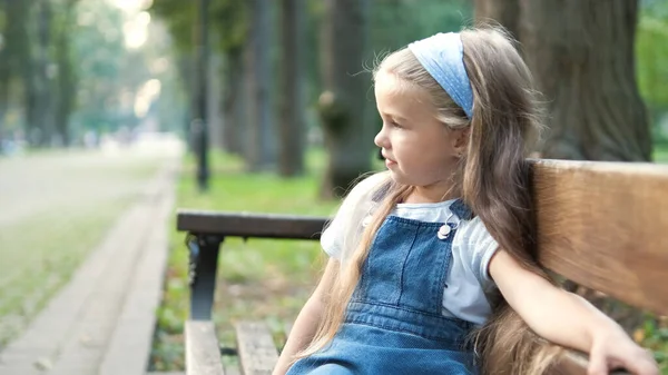 Petite fille assise seule sur un banc dans un parc d'été — Photo
