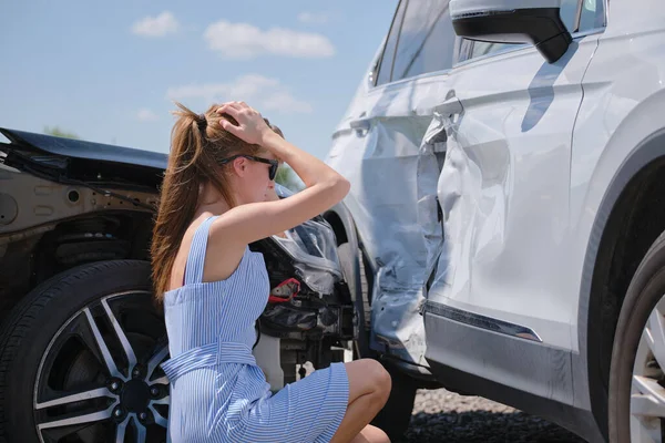 Triste joven conductora sentada cerca de su coche destrozado mirando sorprendido en vehículos estrellados en accidente de tráfico — Foto de Stock